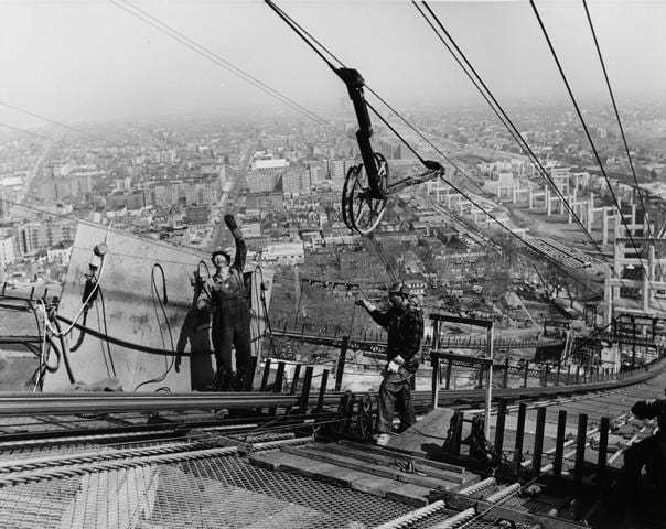 View looking northeast from Brooklyn span. Wheel from spinning cable from Staten Island passing over worker's head. March 25, 1963. Photo: Unknown, 1963, New York City